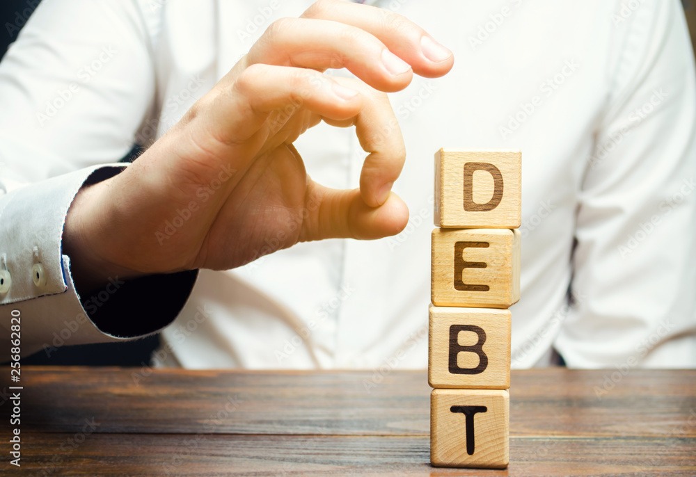 Businessman removes wooden blocks with the word Debt. Reduction or restructuring of debt. Bankruptcy announcement. Refusal to pay debts or loans and invalidate them. Debts service relief